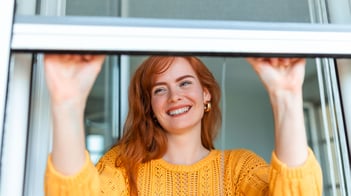 Frau öffnet lachend ein Fenster