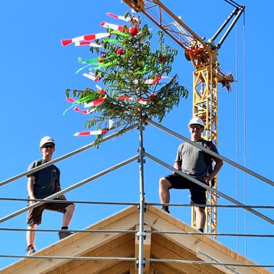 Aufrichte: zwei Mitarbeiter stehen auf dem Dach des fertigen Umbaus