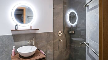 Nachhaltig im Bad: frisch saniertes Bad mit rundem Spiegel und modernem Waschbecken 