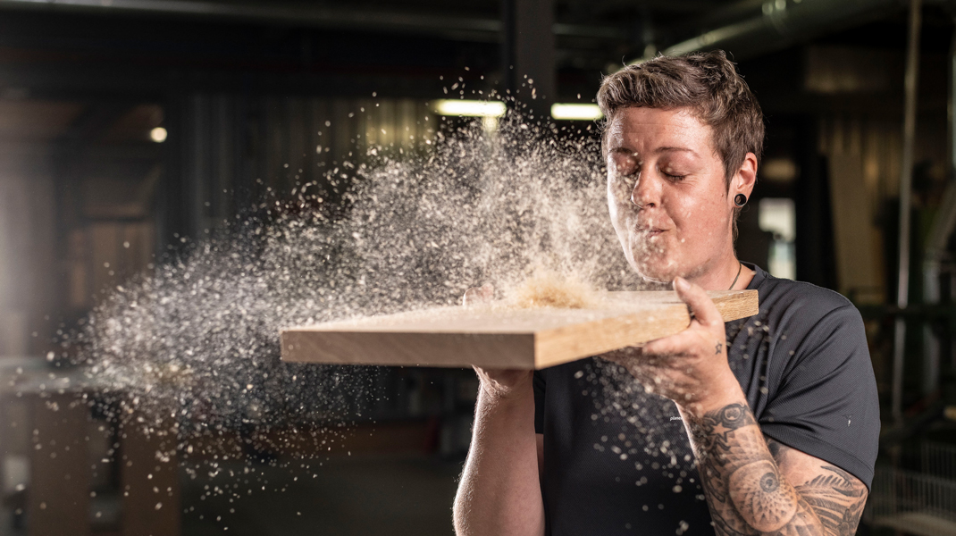 Naturbaustoffe für Ihr Haus, dargestellt mit Schreinerin, die Sägemehl von Holz wegpustet