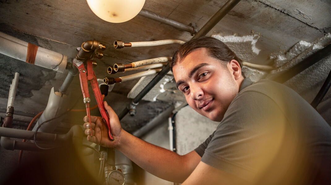 Ozan, der angehende Heizungsinstallateur, ist bei der Arbeit zu sehen und lächelt uns entgegen