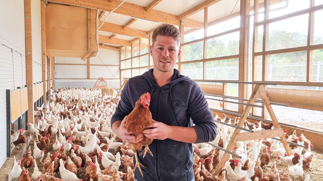 Bauherr ist im Neubau des Legehennenstalls und hält ein glückliches Huhn