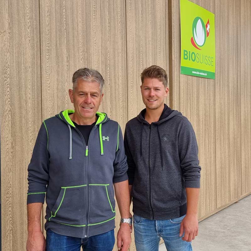 Bauherrschaft, Vater und Sohn stehen vor Neubau des Stalls mit Bio Suisse Logo
