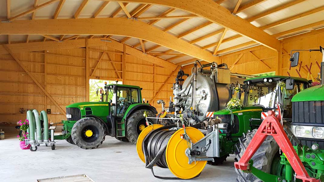 Freitragende Holzhalle gefüllt mit Traktoren und Maschinen.